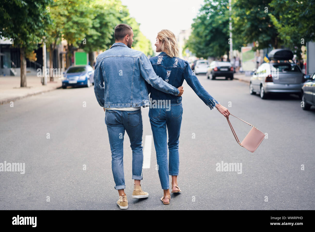 Back view of hugging couple walking away on the street. Love, romance and dating concept Stock Photo