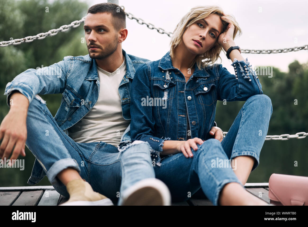 Beautiful fashionable couple posing on river bridge wearing denim jeans. Fashion people, love, emotions and relationship concept Stock Photo