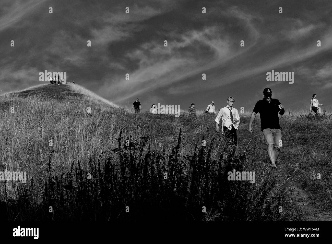 A group of people walking down a hill next to Glastonbury Tor. Stock Photo