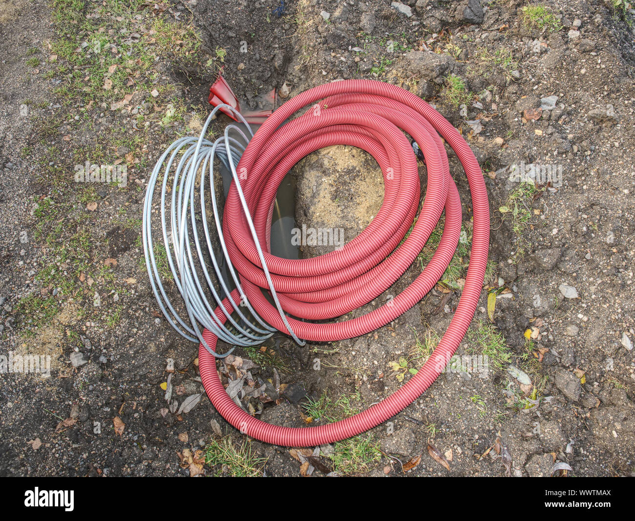 Thin diameter ribbed orange PVC pipe in the ground before laying Stock