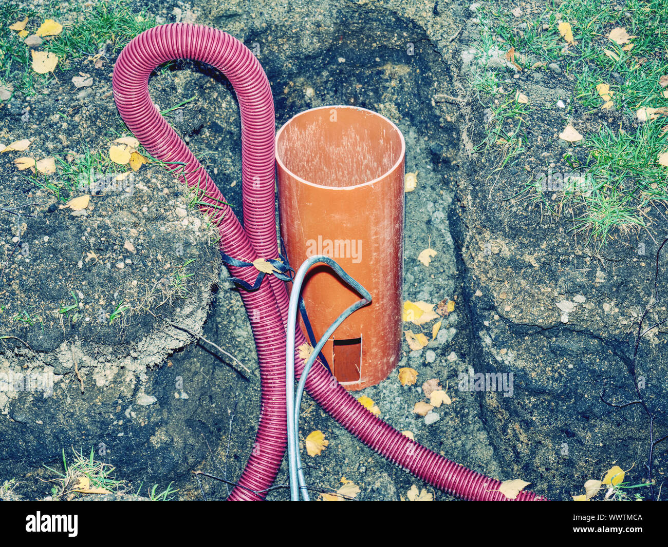 Thin diameter ribbed orange PVC pipe in the ground before laying Stock