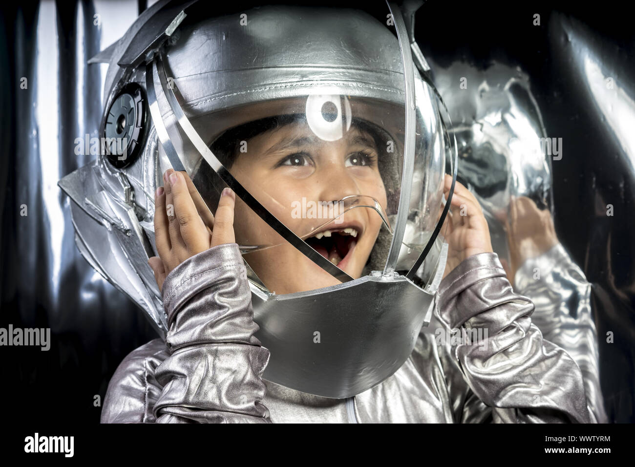 Imagination, Boy playing to be an astronaut with a space helmet and silver  suit on metallic background Stock Photo - Alamy