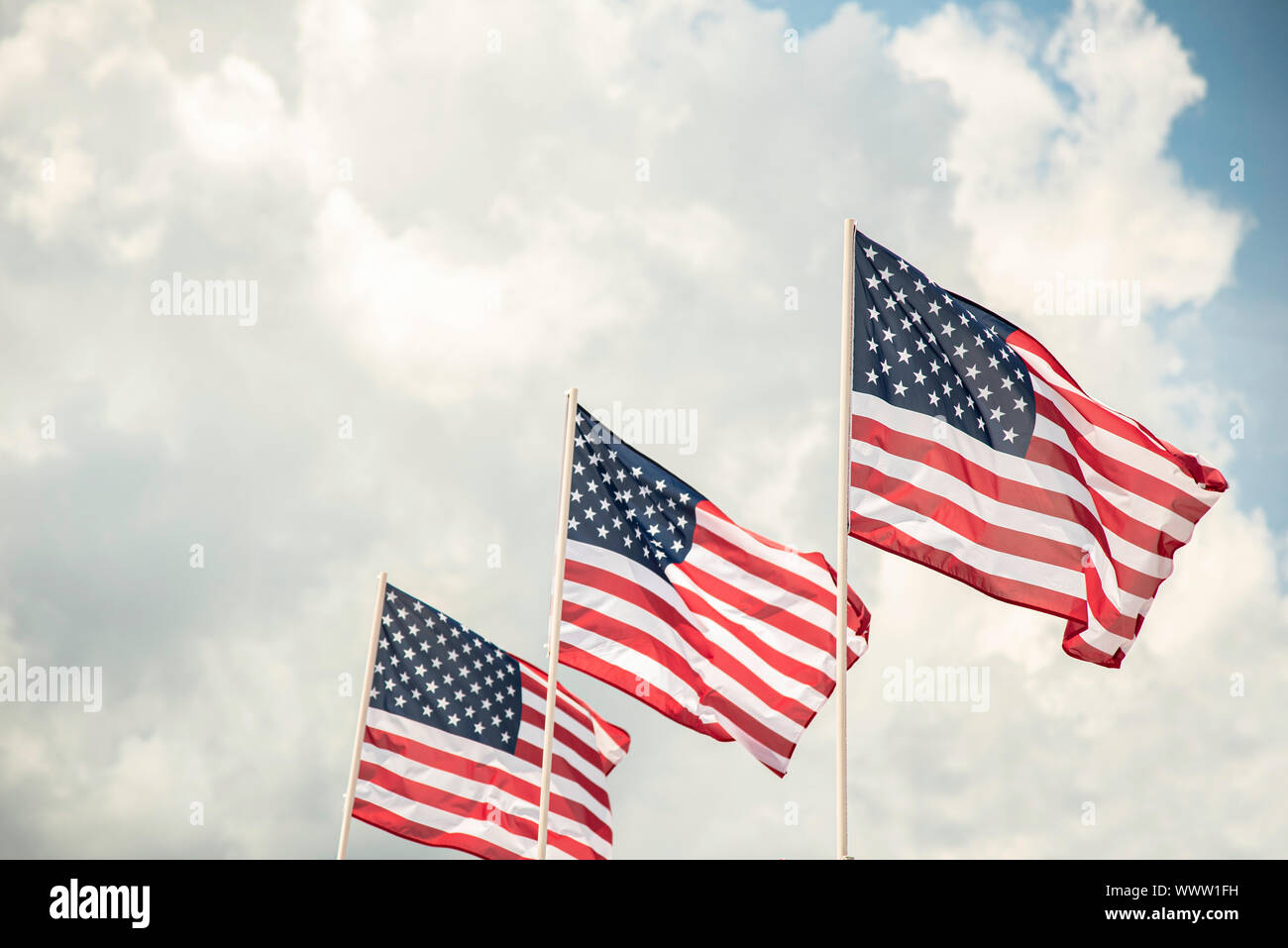 Three American flags fluttering in the wind against a bright blue sky ...