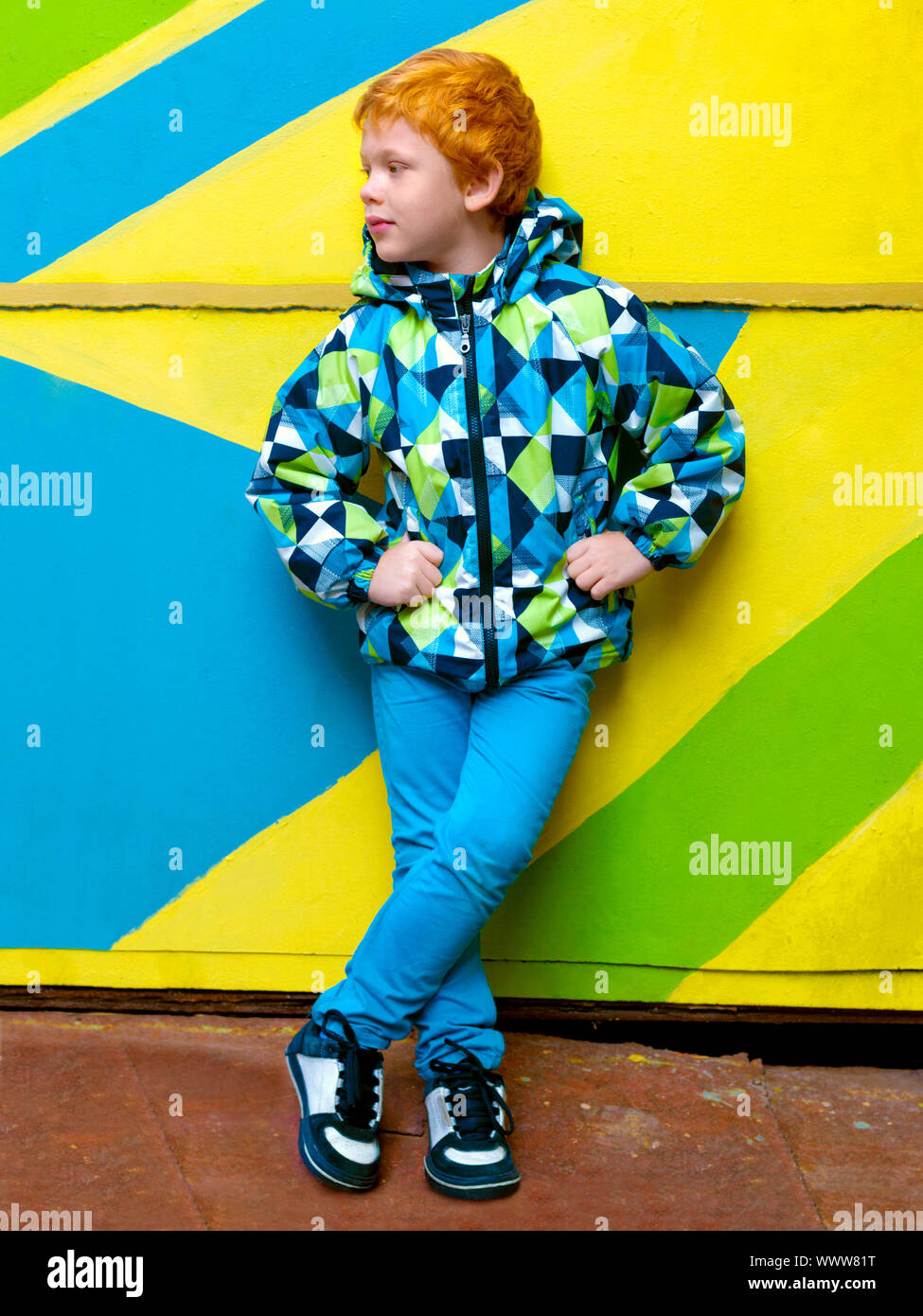 Fashionable little boy. Red-haired handsome kid. Model wearing trendy jacket posing against striped wall background enjoying good autumn-spring Stock Photo