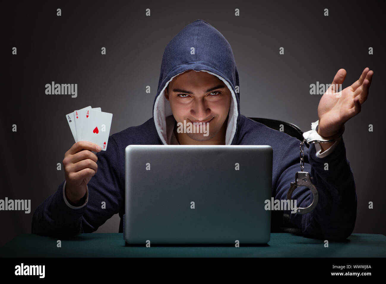 Young man in handcuffs wearing a hoodie sitting in front of a la Stock Photo