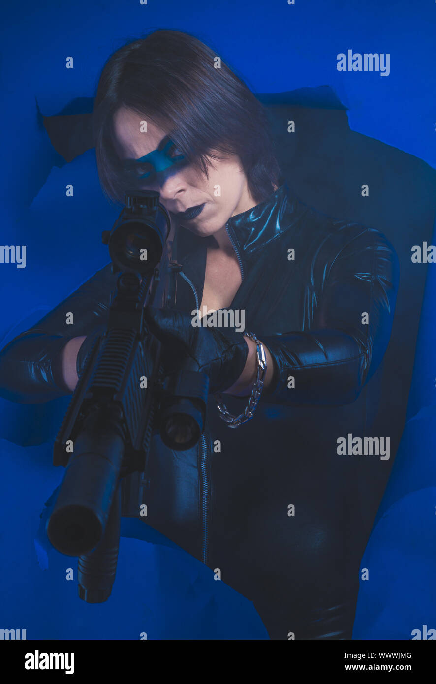 Soldier, Brunette girl dressed in leather and latex fitted with pistol on blue background Stock Photo