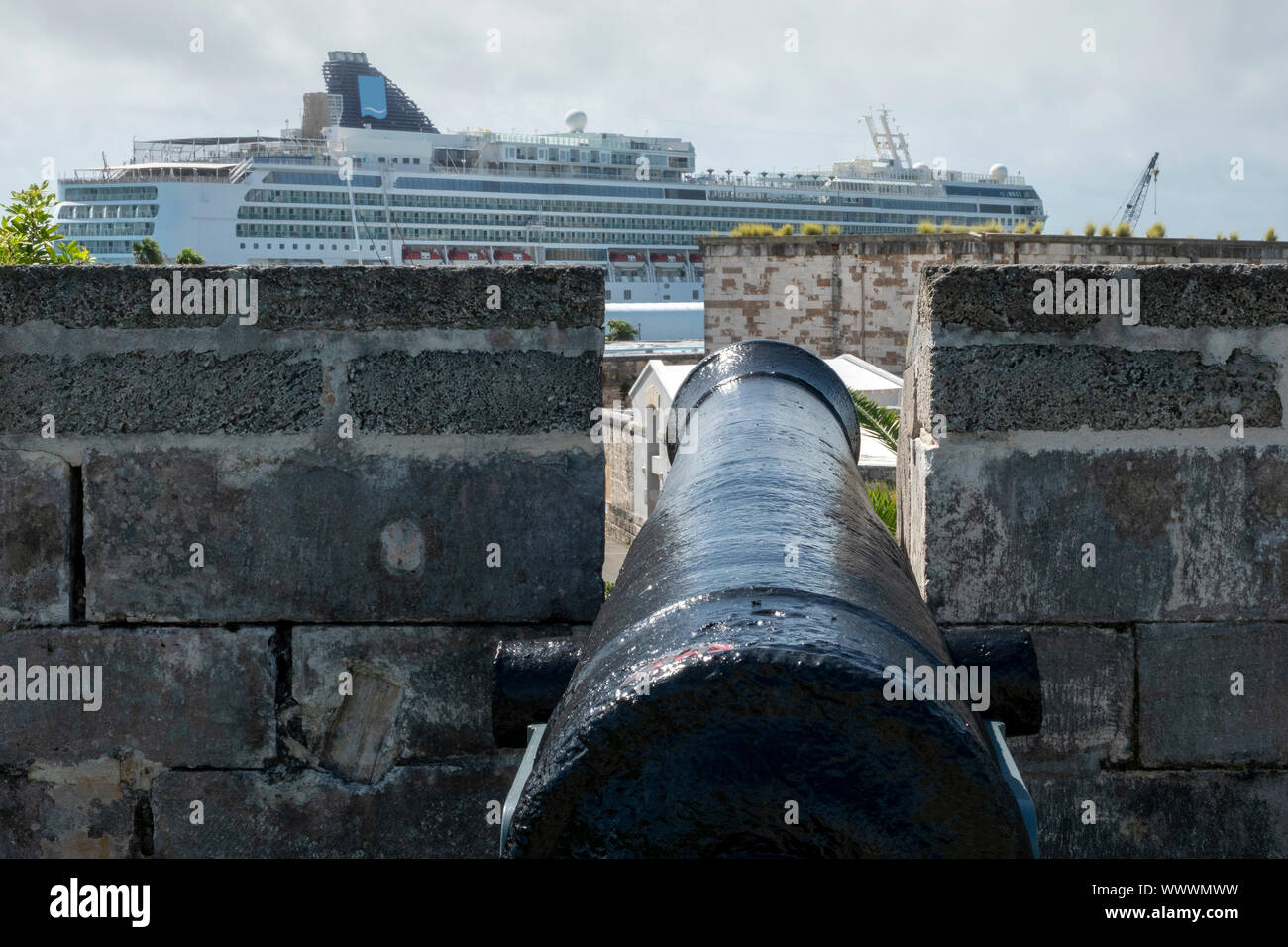 A battlement mounted muzzle loading cannon aiming at a cruise ship at The Royal Naval Dockyard, Bermuda Stock Photo