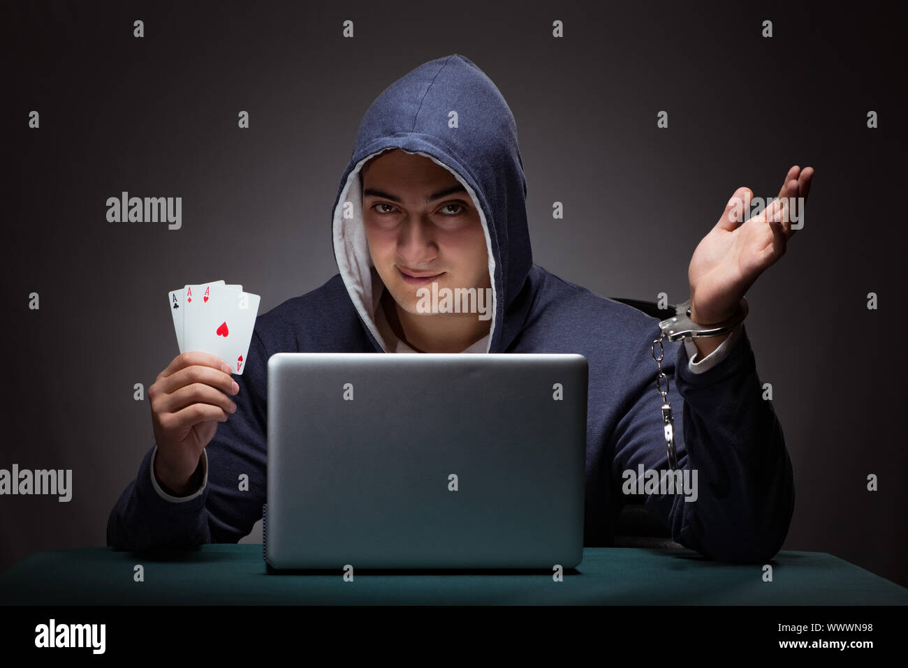 Young man in handcuffs wearing a hoodie sitting in front of a la Stock Photo