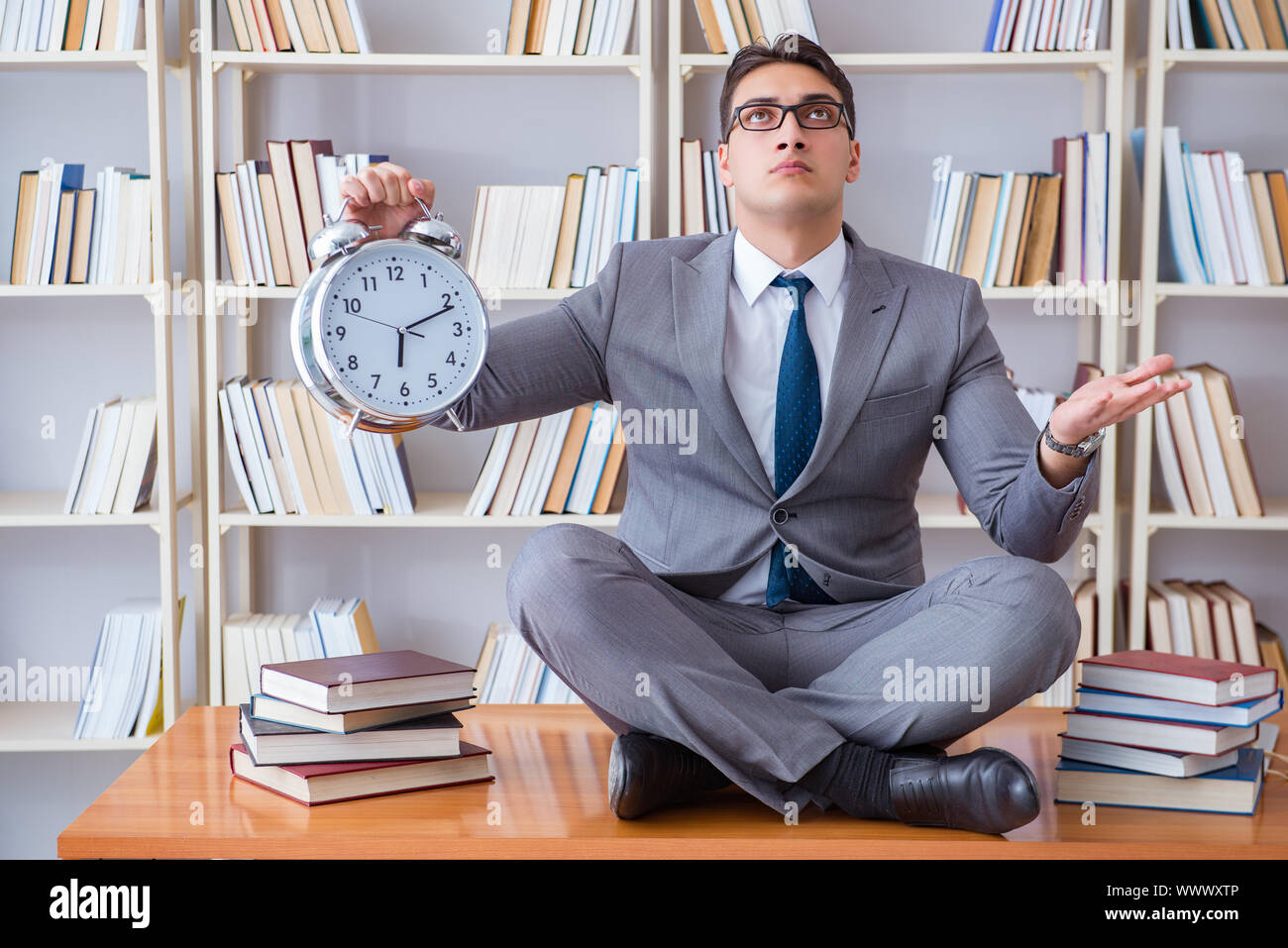 Businessman student in lotus position with an alarm clock in lib Stock Photo