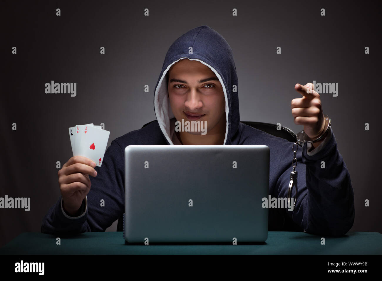 Young man in handcuffs wearing a hoodie sitting in front of a la Stock Photo