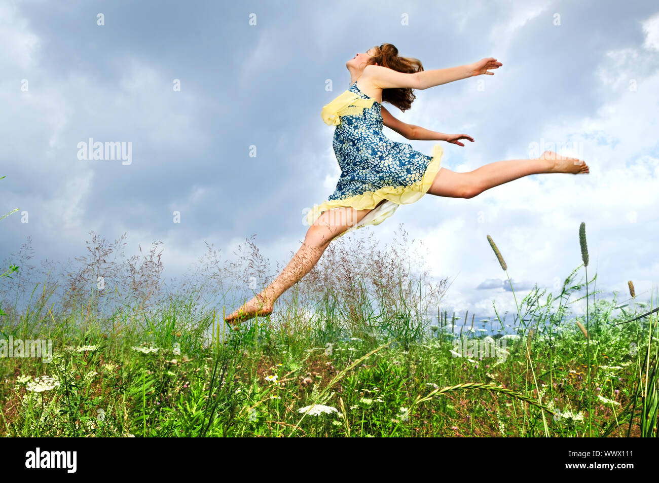 Young teenage girl jumping in summer meadow amid wildflowers Stock Photo