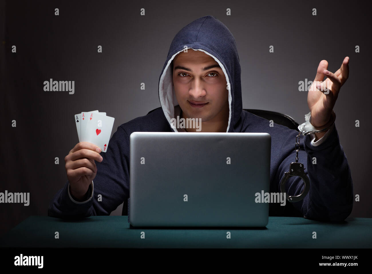 Young man in handcuffs wearing a hoodie sitting in front of a la Stock Photo
