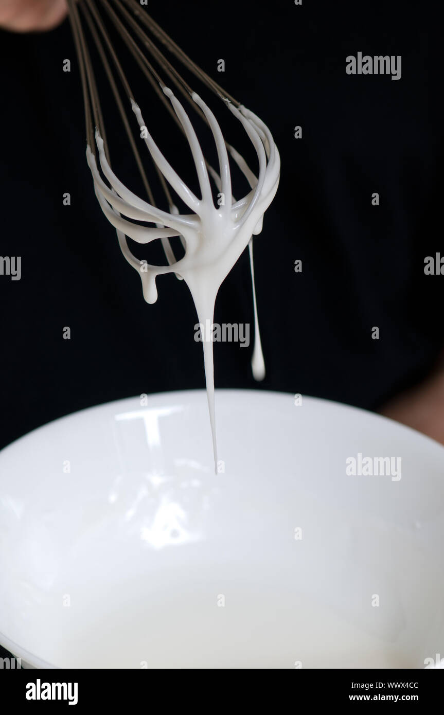Whisk with creamy egg white close up over white bowl Stock Photo