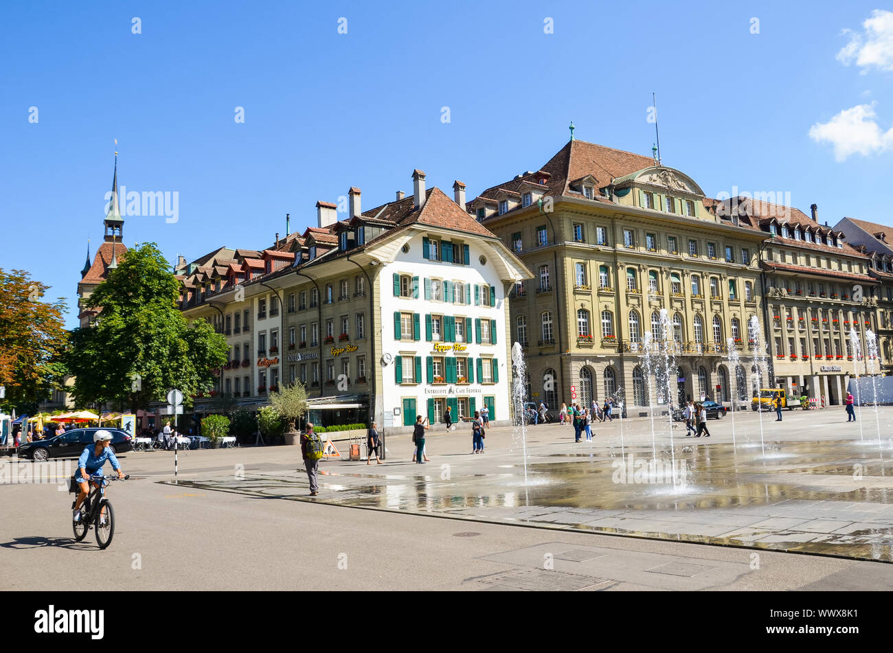 Bern, Switzerland - August 14, 2019: Bundesplatz, the square in the city center of the Swiss capital with people walking. Historical buildings, cafes, restaurants. Water fountains. Sunny summer day. Stock Photo