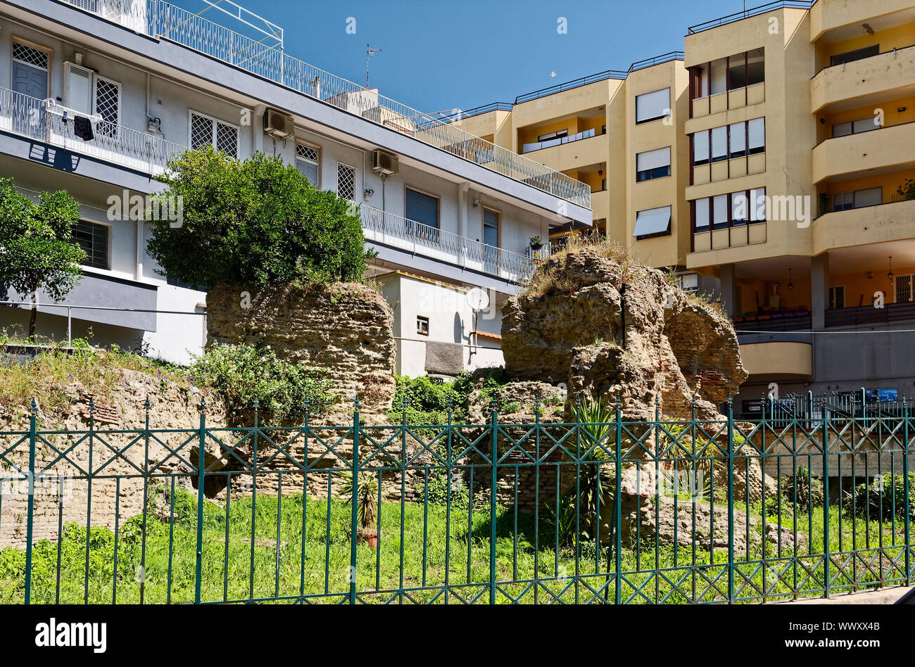 Roman ruins, modern apartment buildings; old and new; contrast; metal fence, vegetation, city neighborhood, Pozzouli; Italy; Europe; spring; horizonta Stock Photo