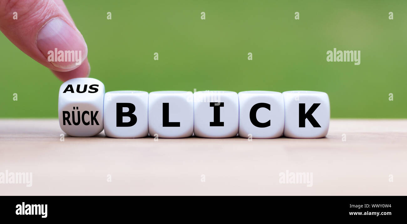 Hand turns a dice and changes the German word 'Rückblick' ('review' in English) to 'Ausblick' ('Outlook' in English). Stock Photo