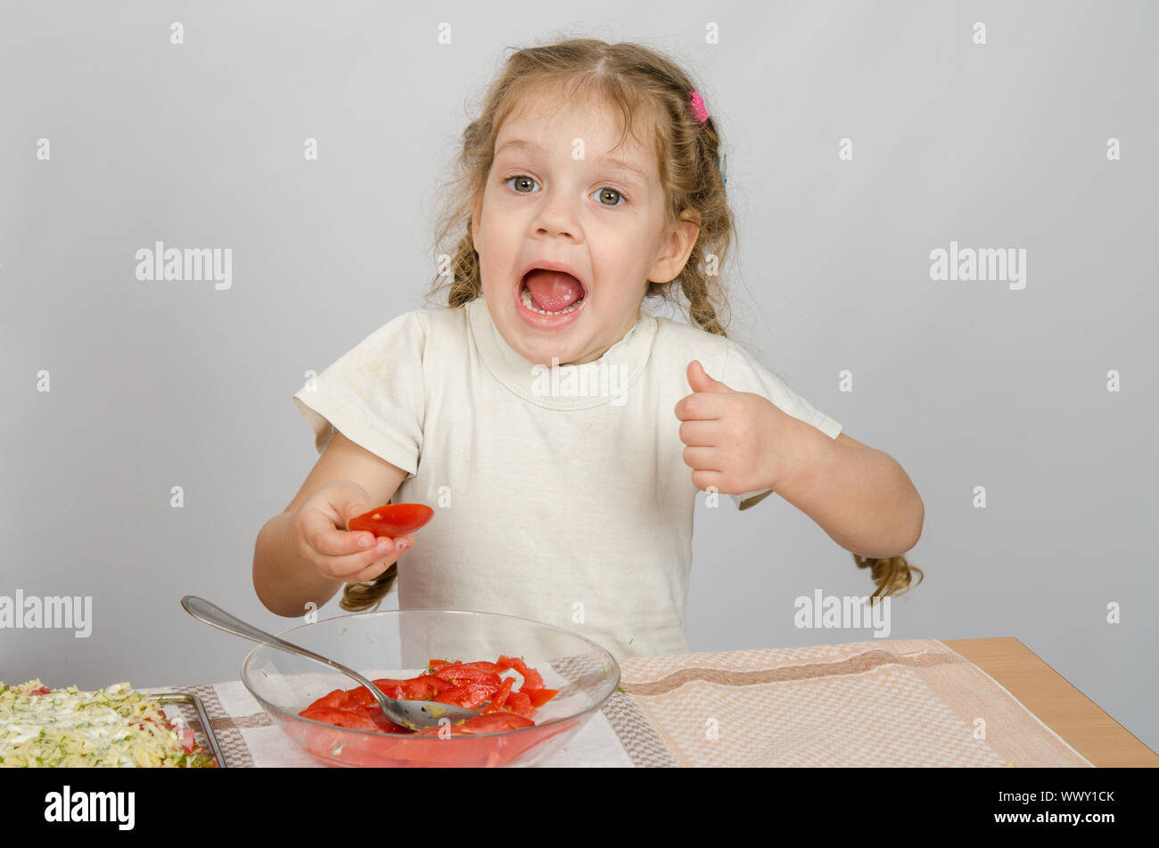 Little girl with mouth open holding a large slice of tomato Stock Photo