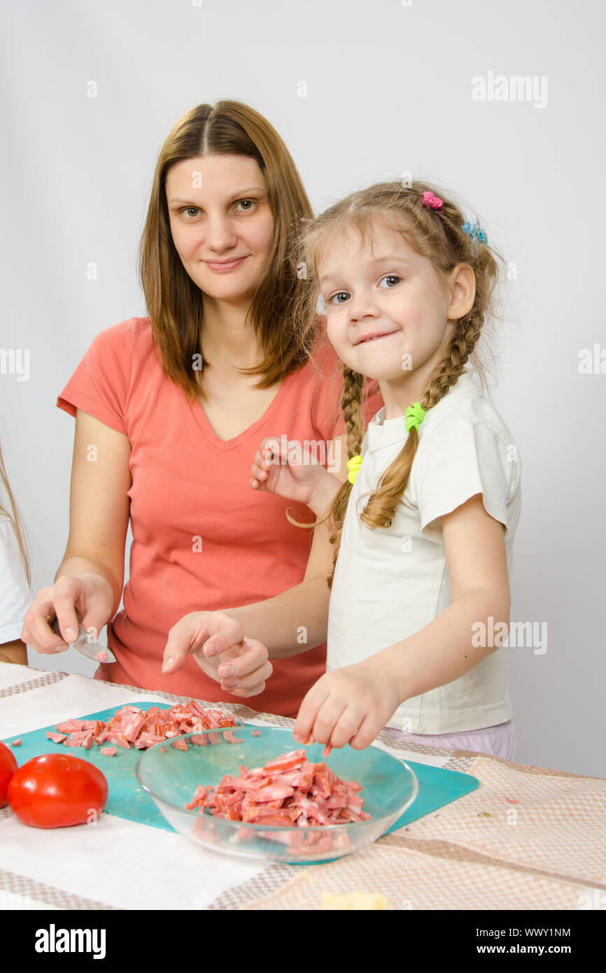 Little six year old girl helps mother to cook at the kitchen table