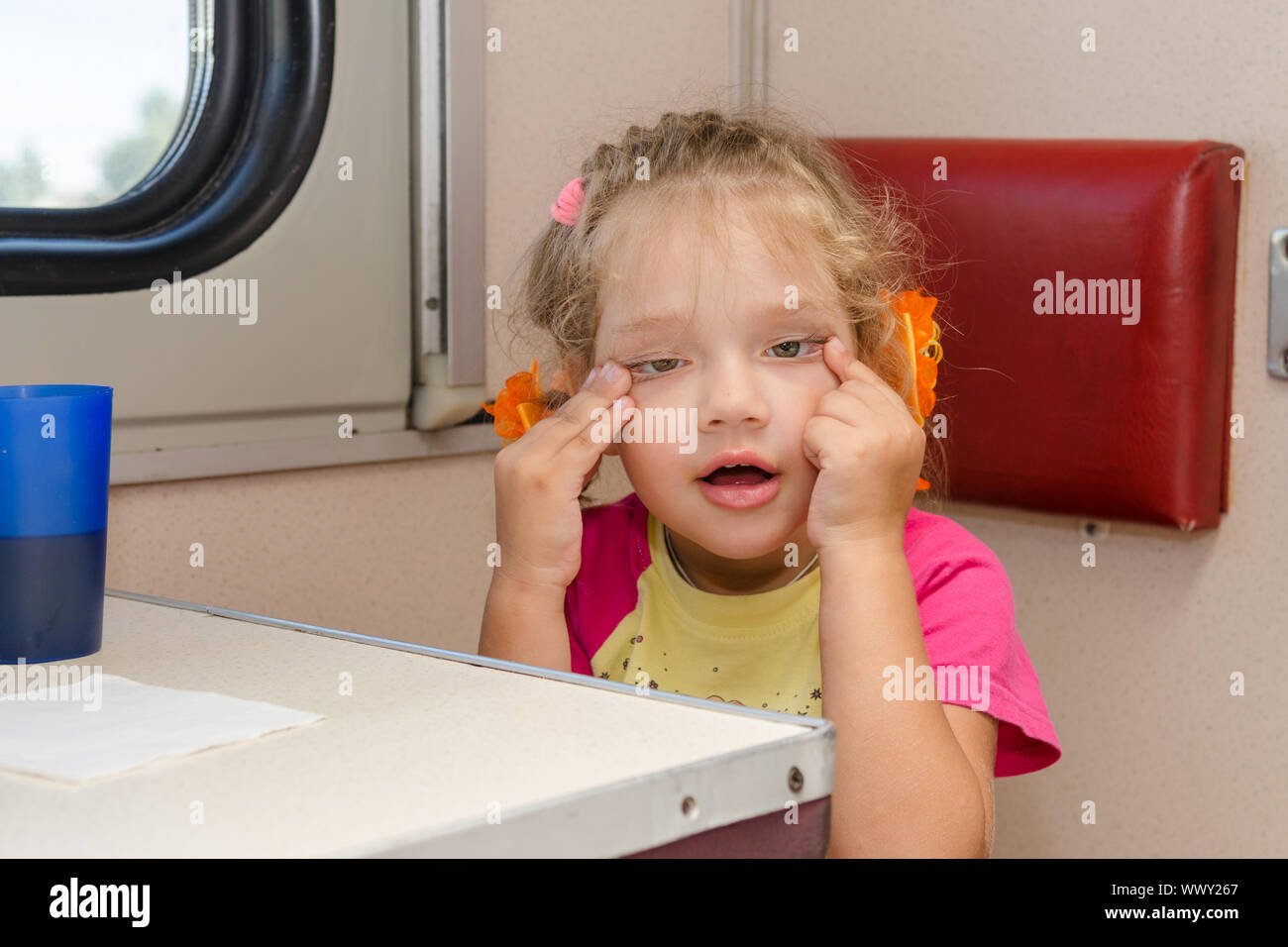 Girl makes faces four years of sitting on the train at the table on the side a place reserved seat Stock Photo