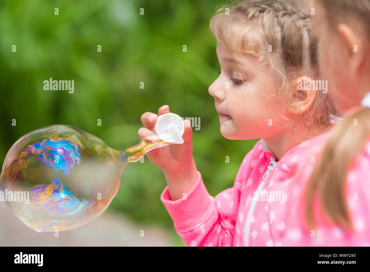Five-year girl inflates a large bubble, another girl with interest looks at her Stock Photo