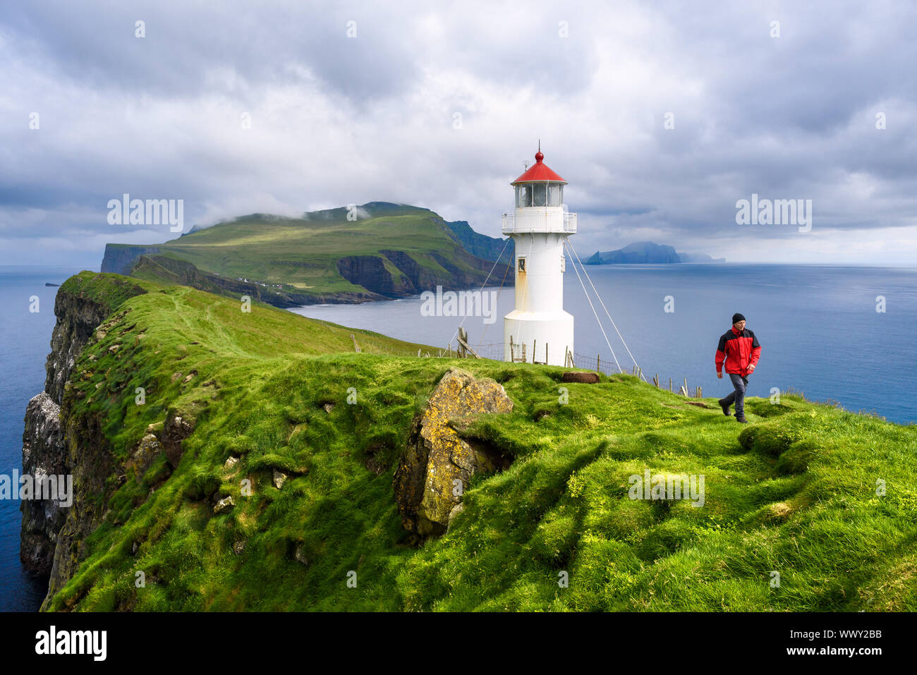 Mykinesholm islet lighthouse near Mykines island. Mykinesholmur, Faroe islands. Tourist in red jacket explores attractions. Summer landscape Stock Photo