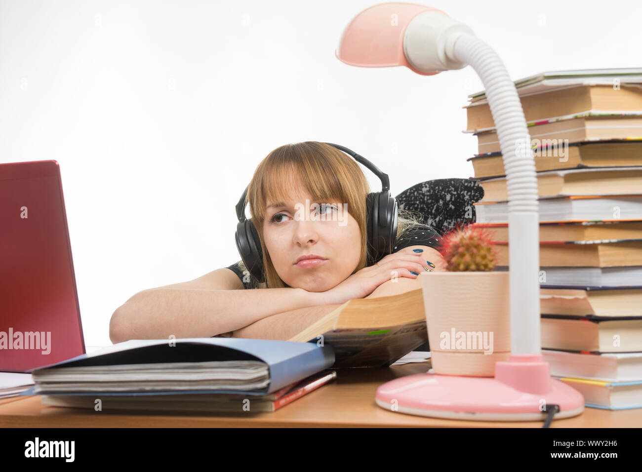 Girl sad student sitting at the table wearing headphones and listening to music Stock Photo