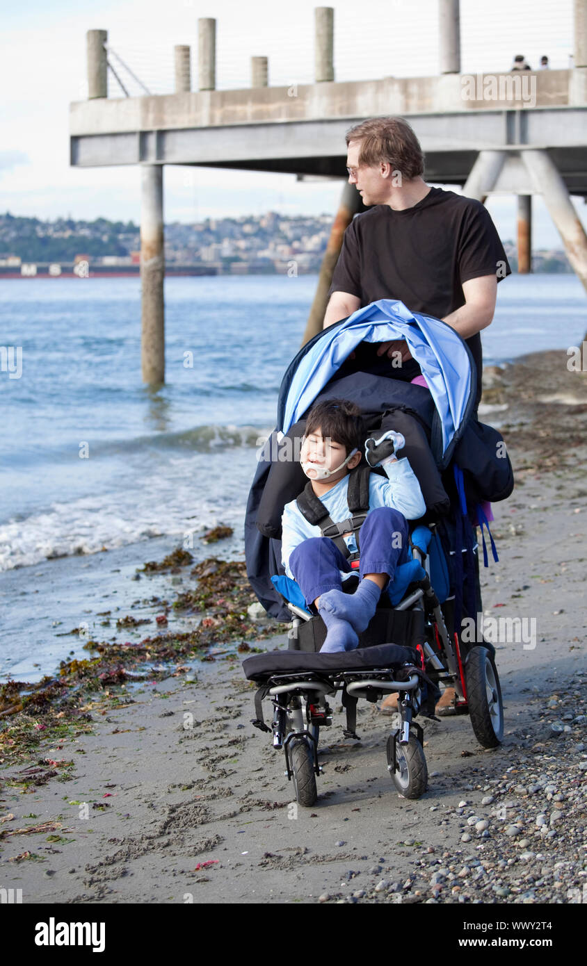 Father pushing wheelchair with disabled son on beach Stock Photo