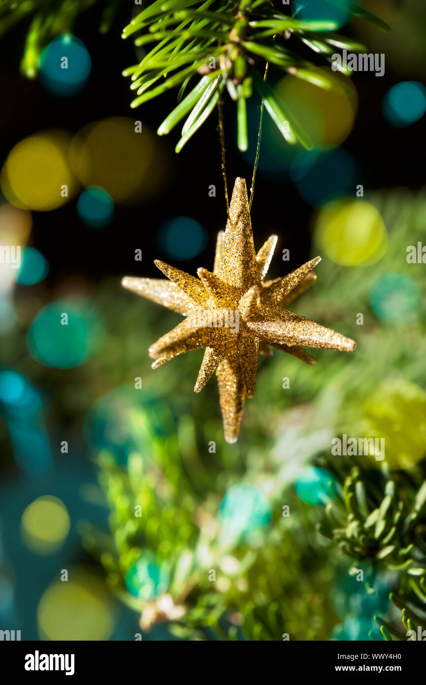 Decorative Gold Star ornament in a Christmas tree in front of a glitter ...