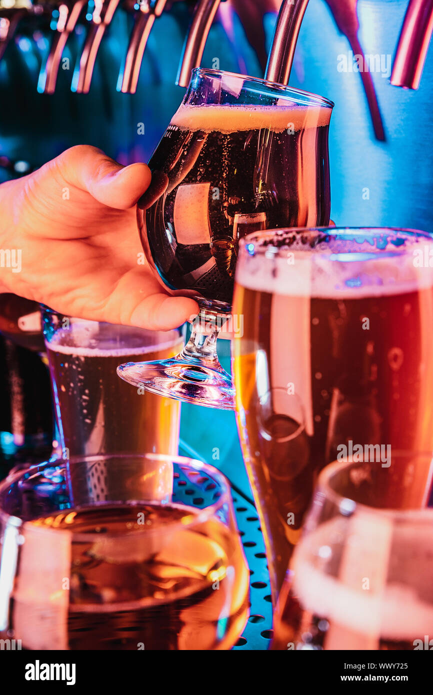Hand of bartender pouring a large lager beer in tap. Bright and modern neon light, males hands
