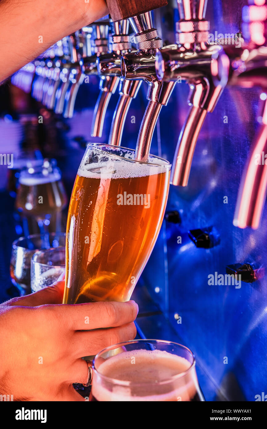 Hand of bartender pouring a large lager beer in tap. Bright and modern neon light, males hands