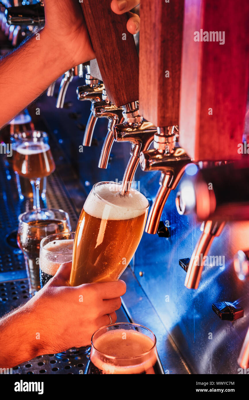 Hand of bartender pouring a large lager beer in tap. Bright and modern neon light, males hands