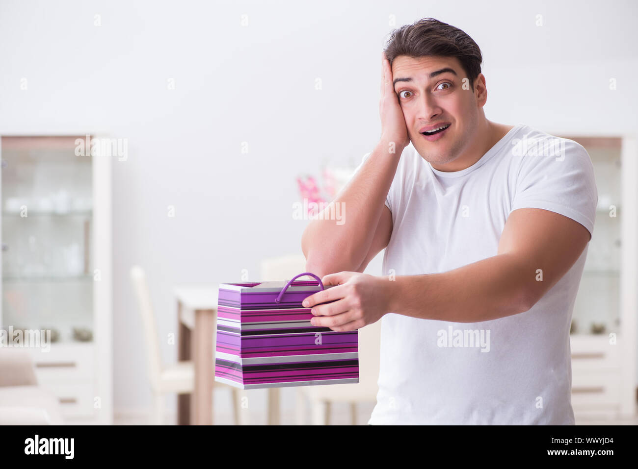 Young man with gift bag at home preparing suprise for wife Stock Photo