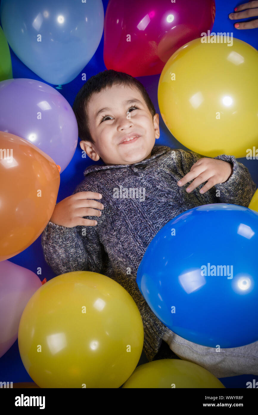 childhood, Brunette boy playing with a lot of colorful balloons, smiles and joy at birthday party Stock Photo