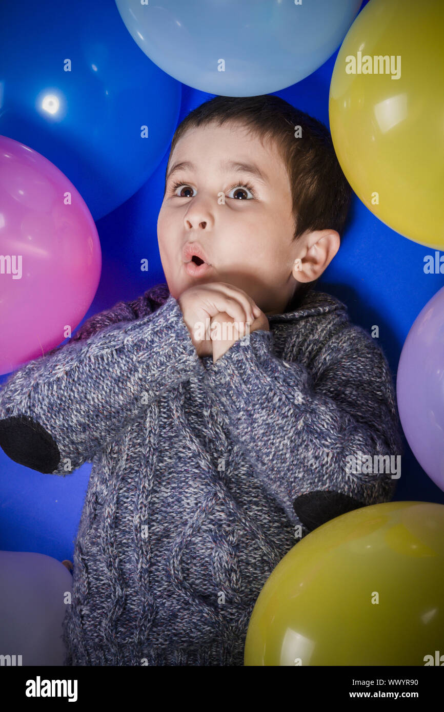 Brunette boy playing with a lot of colorful balloons, smiles and joy at birthday party Stock Photo