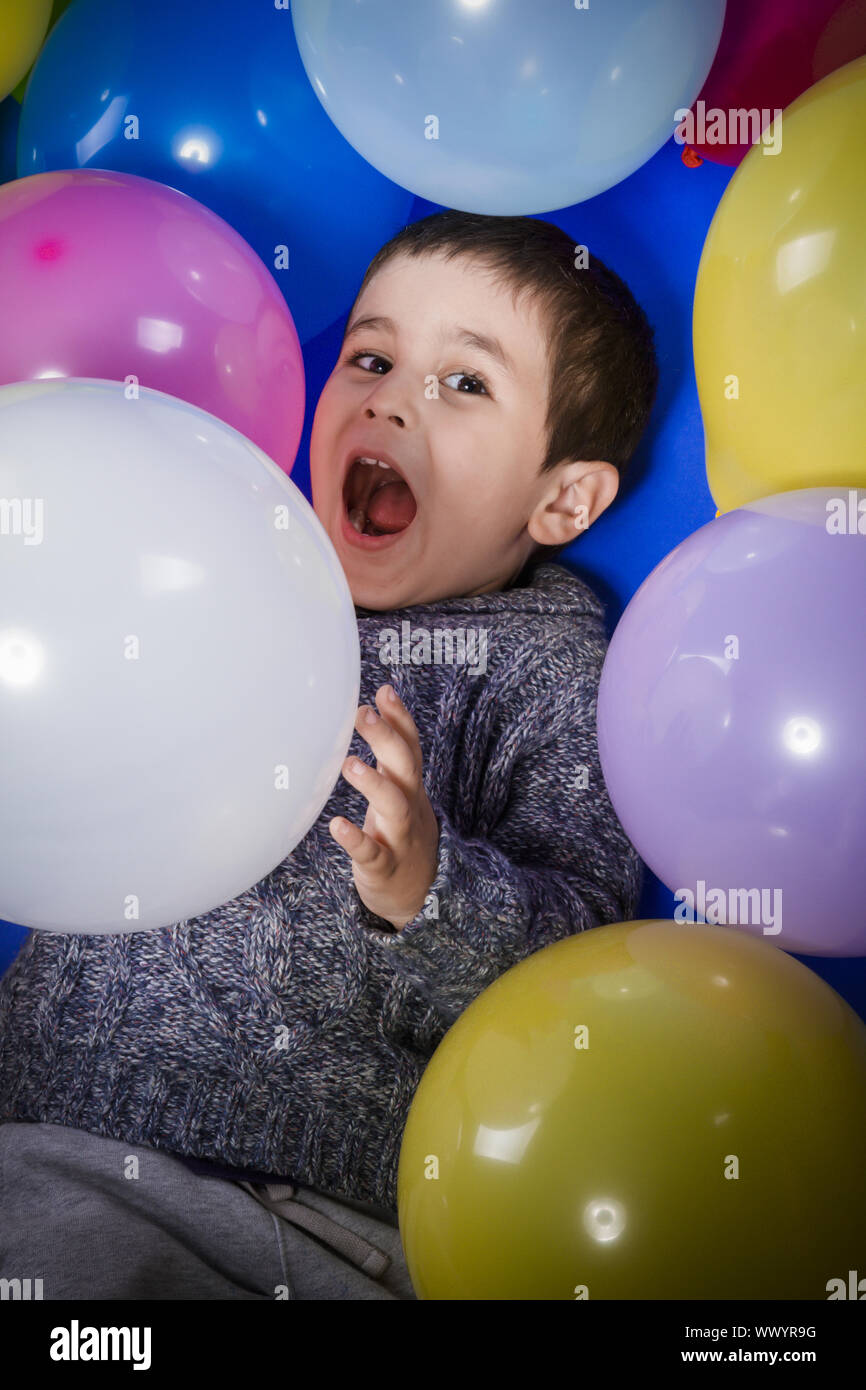 Brunette boy playing with a lot of colorful balloons, smiles and joy at birthday party Stock Photo