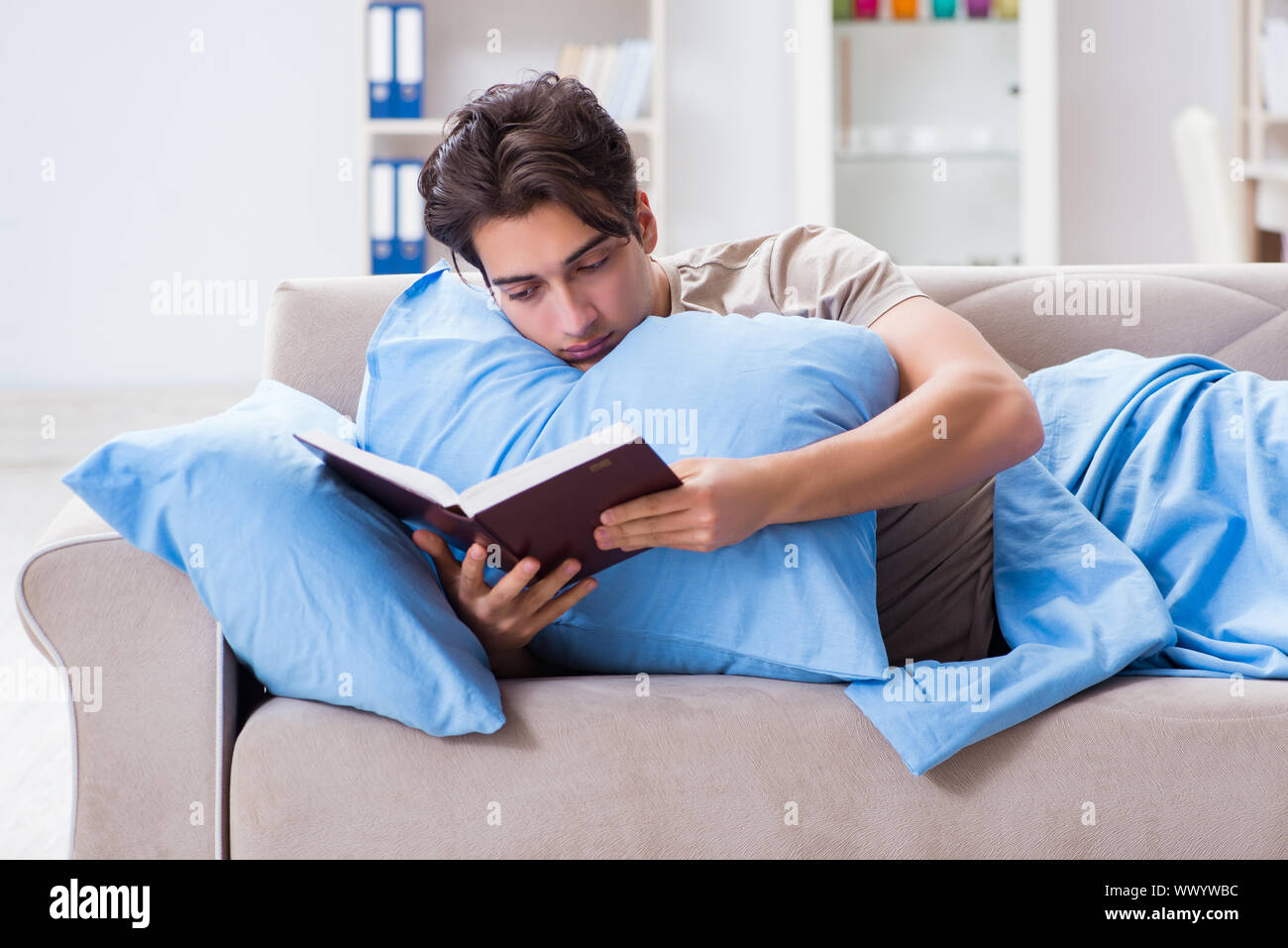 Young student man preparing for college exams in bed with book Stock