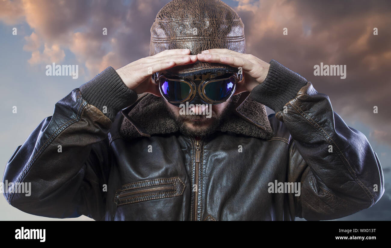 pilot of the 20s with sunglasses and vintage aviator helmet. Wears leather jacket, beard and expressive faces Stock Photo