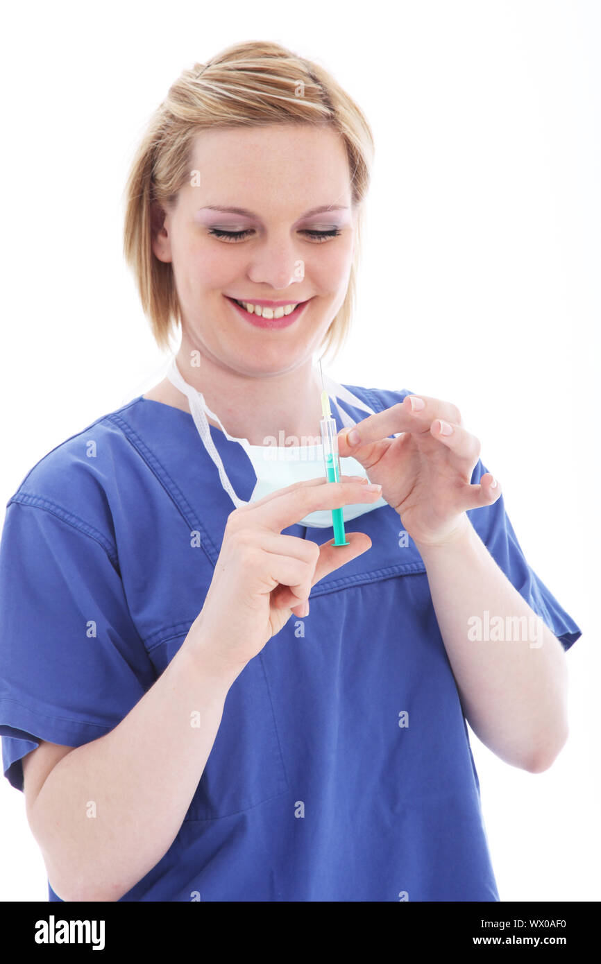 Happy smiling nurse wearing blue scrubs preparing an injection by flicking the syringe to free and expel trapped air bubbles Stock Photo