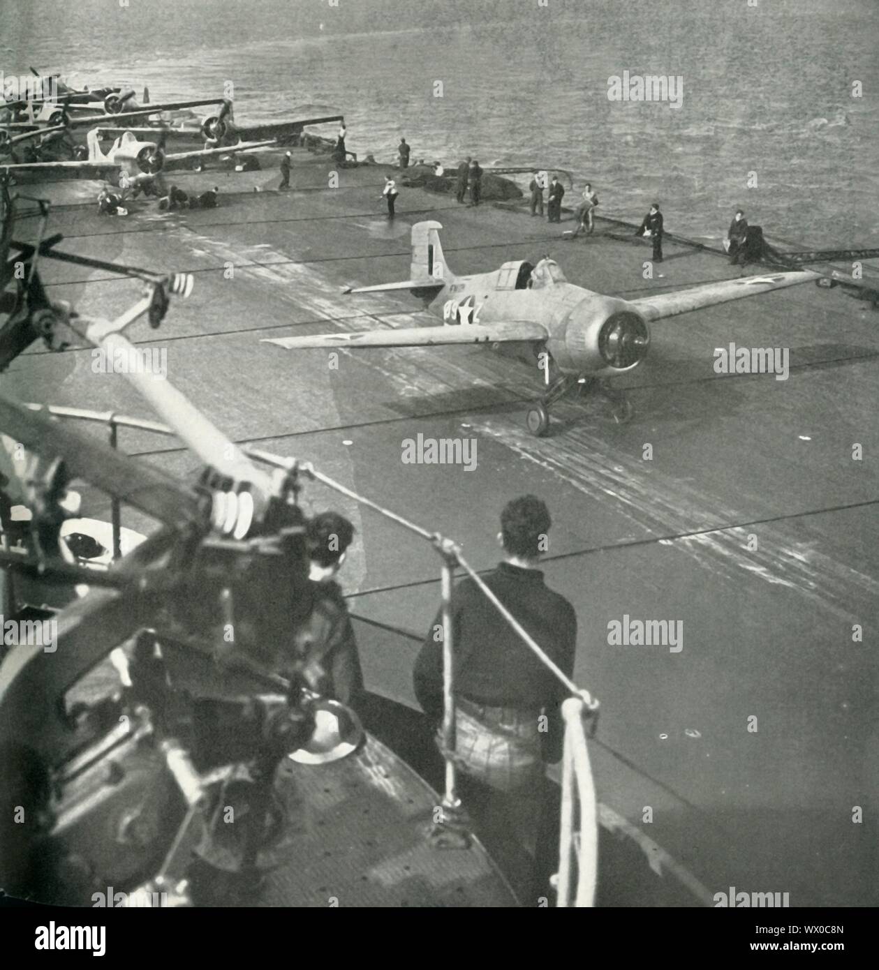 Fighter planes on board an aircraft carrier, Second World War, c1943. 'A Martlet [Grumman F4F Wildcat] of the Fleet Air Arm, bearing American markings, flies off a British carrier during the African operations, while other Martlets and Seafires are ready to follow. The Fleet Air Arm protected the [Royal Navy] Fleet and transports, covered the landings, and supported the advance.' The FAA is the section of the Royal Navy responsible for the operation of naval aircraft. From &quot;Fleet Air Arm&quot;. [His Majesty's Stationery Office, London, 1943] Stock Photo