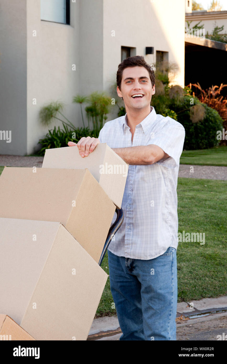 A happy male looking at the camera pushing a dolly with moving boxes Stock Photo
