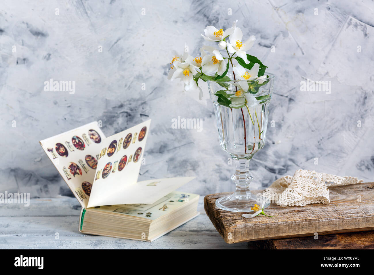 Sprigs of jasmine in a glass and an open old book. Stock Photo