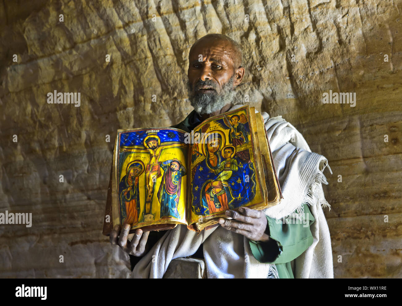 Orthodox priest of the rock church Mikael Mellehayzengi shows liturgical book, Tigray, Ethiopia Stock Photo