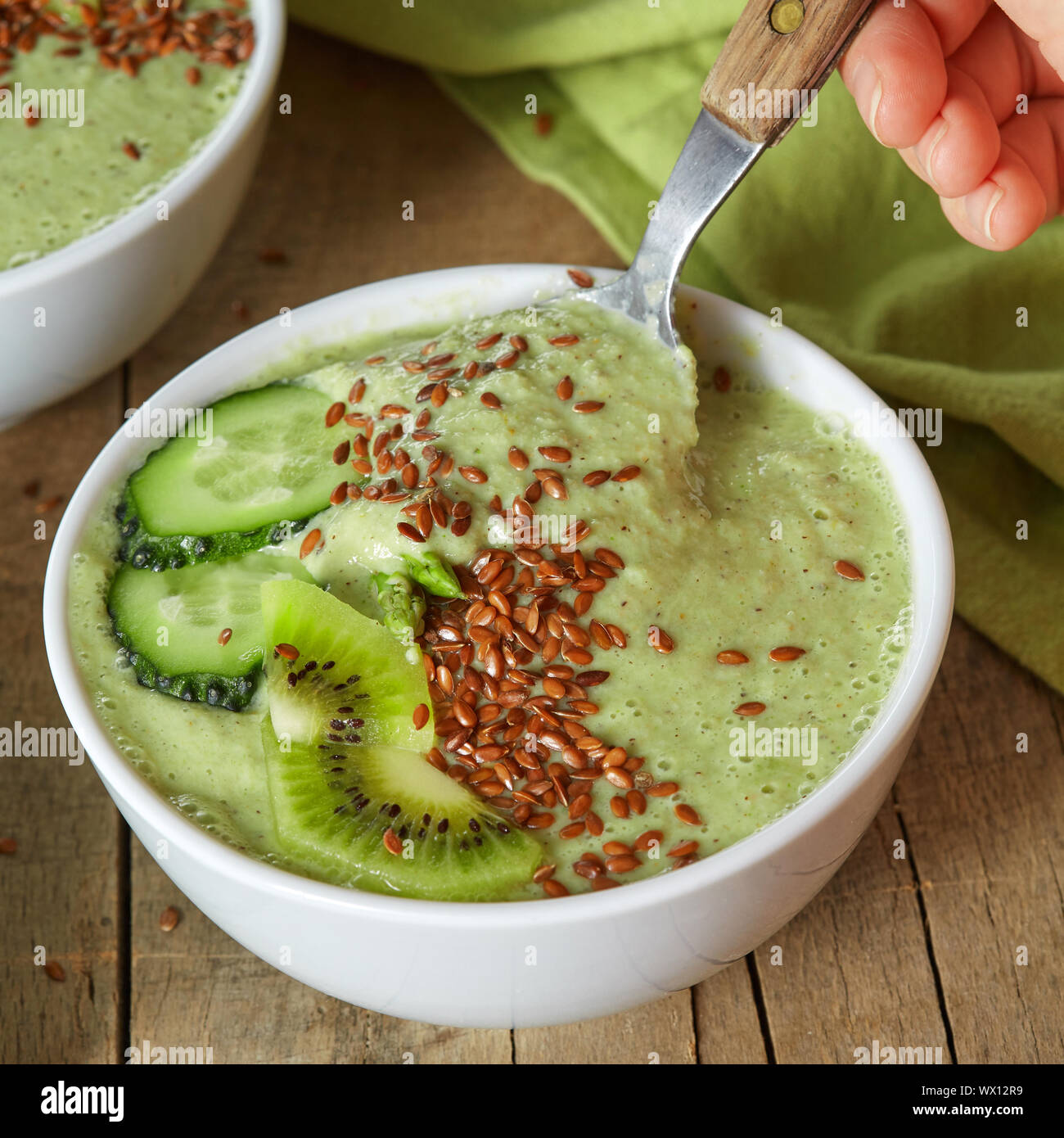 In a plate with green smoothies with flax seeds, a female hand dropped a spoon on wooden background Stock Photo