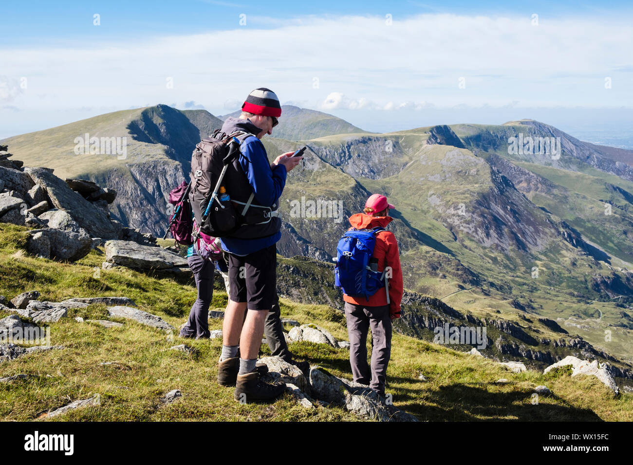 A hiker looks at a GPS device whilst hiking on Glyder Fach in Snowdonia National Park with view of mountains above Ogwen Conwy north Wales UK Britain Stock Photo