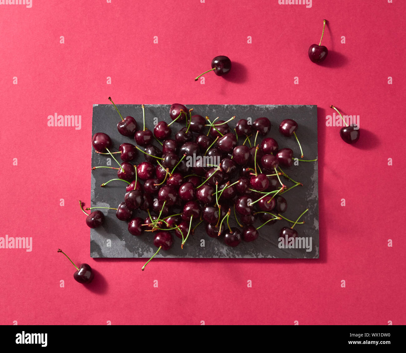 Delicious sweet cherry on a black stone board on red paper background with place for text. Flat lay. Stock Photo