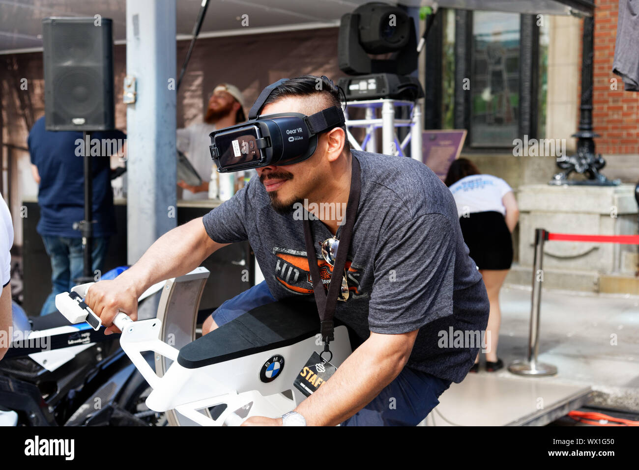A man wearing virtual reality goggles and riding a motorcycle simulator Stock Photo