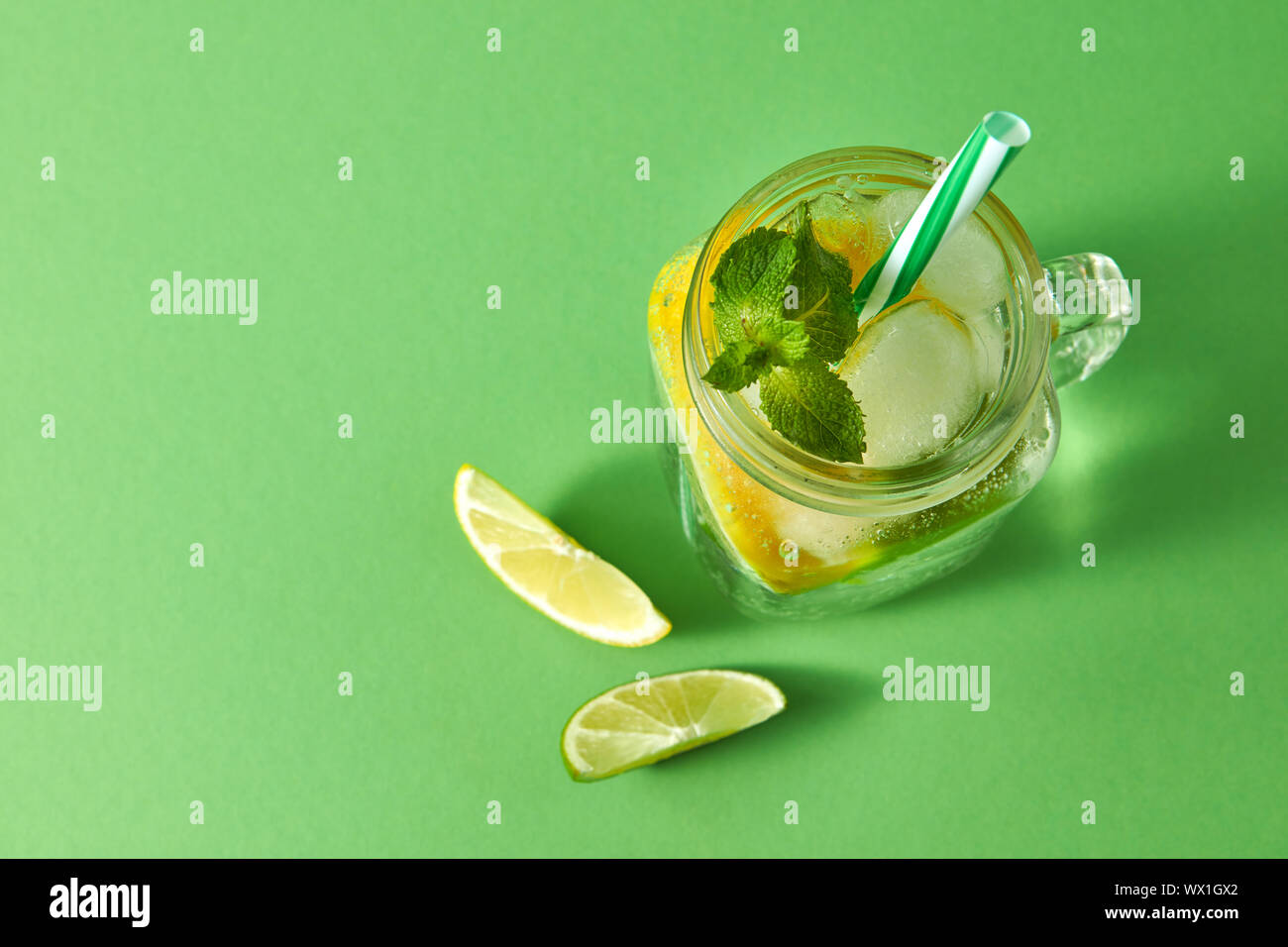 Refreshing homemade sparkling lemonade with ice in mason jar, slices of lime and lemon, leaf of ...