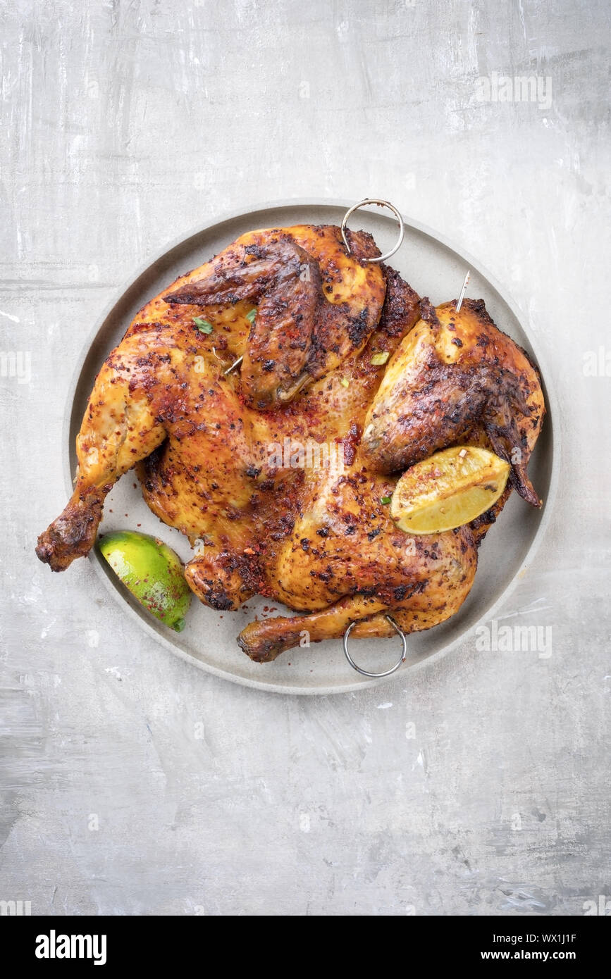 Spatchcocked barbecue chicken al mattone with lemon slices as top view on a plate Stock Photo