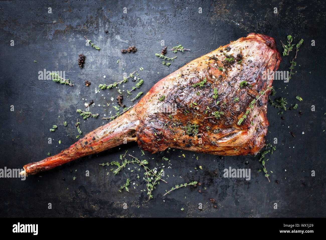 Marinated barbecue aged leg of venison with herbs as top view on a rustic board Stock Photo