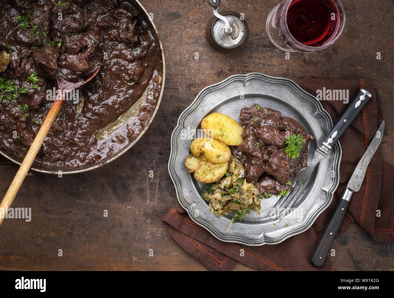 Fresh veal liver ragout in red wine sauce with fried potatoes and cabbage as top view on a plate